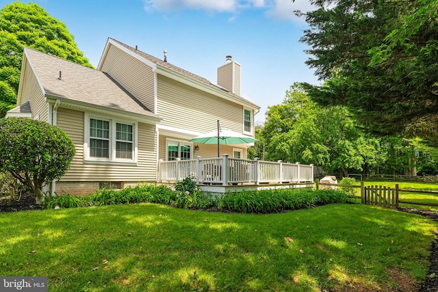 rear view of property with roof with shingles, a yard, a chimney, fence, and a deck