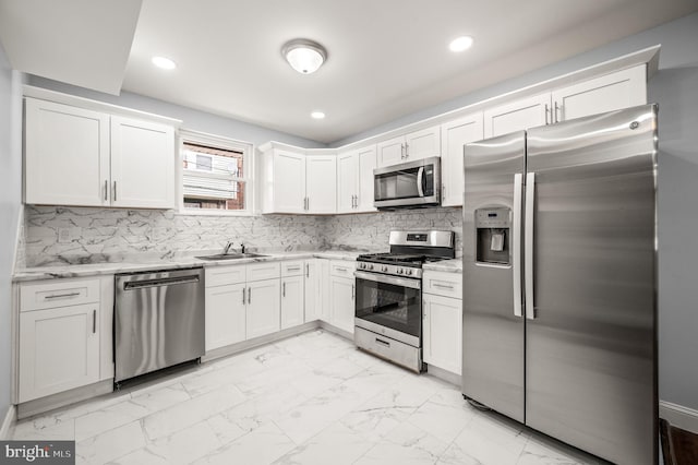 kitchen featuring sink, light stone counters, appliances with stainless steel finishes, decorative backsplash, and white cabinets