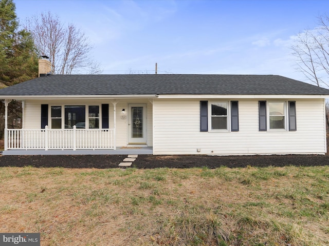 view of front facade with a porch, a chimney, a front yard, and a shingled roof