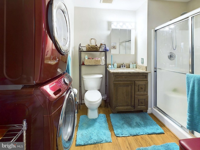 bathroom with toilet, a shower with shower door, stacked washer / drying machine, hardwood / wood-style floors, and vanity