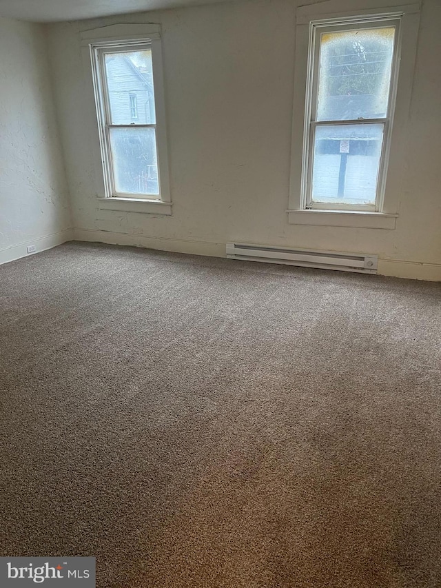 carpeted empty room featuring a baseboard heating unit