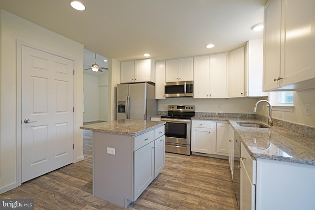 kitchen featuring white cabinets, a kitchen island, wood finished floors, stainless steel appliances, and a sink