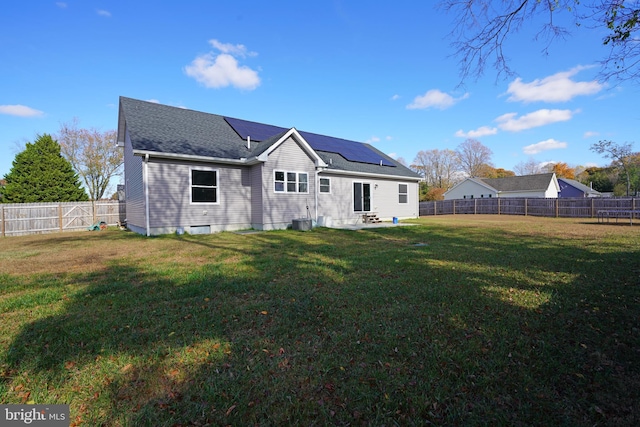 back of house with a fenced backyard, roof mounted solar panels, roof with shingles, and a yard