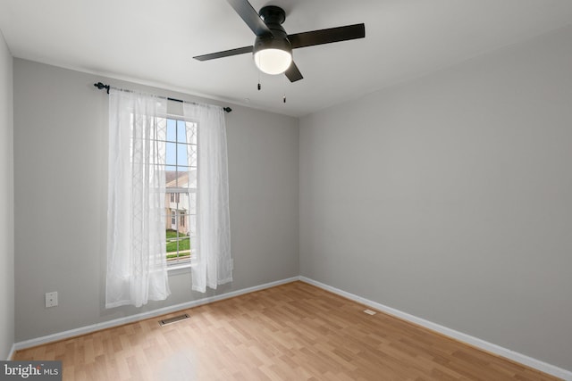 spare room with baseboards, light wood-style flooring, visible vents, and a wealth of natural light