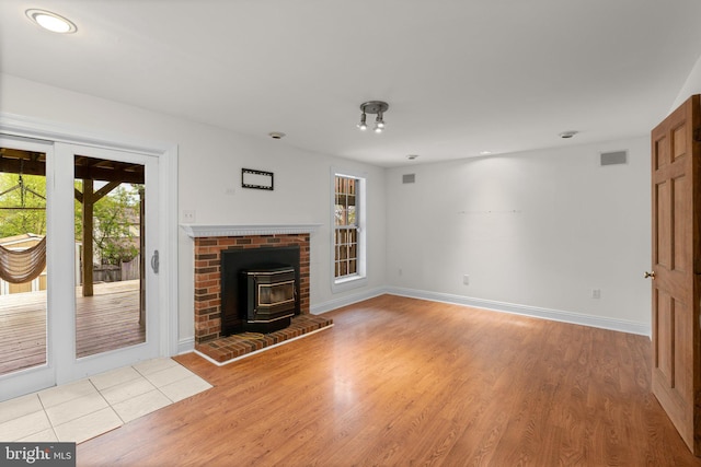 unfurnished living room featuring a wood stove, plenty of natural light, visible vents, and light wood-type flooring