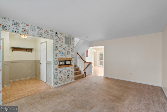 carpeted empty room with baseboards, an inviting chandelier, wallpapered walls, wood finished floors, and stairway