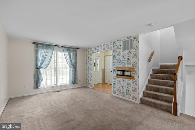 unfurnished living room featuring stairs, wallpapered walls, carpet, baseboards, and visible vents