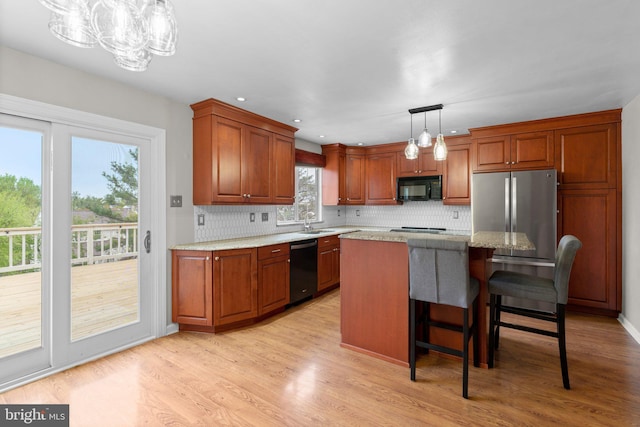 kitchen featuring a sink, black appliances, decorative backsplash, light wood-style floors, and pendant lighting