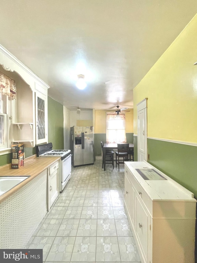 kitchen featuring gas range gas stove, white cabinetry, ceiling fan, and stainless steel fridge with ice dispenser