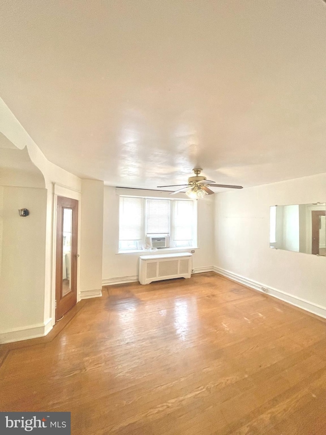 unfurnished living room featuring hardwood / wood-style flooring, ceiling fan, cooling unit, and radiator heating unit