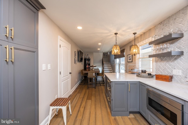 kitchen with gray cabinets, stainless steel microwave, decorative light fixtures, backsplash, and light hardwood / wood-style floors