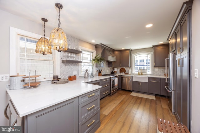 kitchen featuring appliances with stainless steel finishes, decorative backsplash, hanging light fixtures, kitchen peninsula, and light hardwood / wood-style flooring