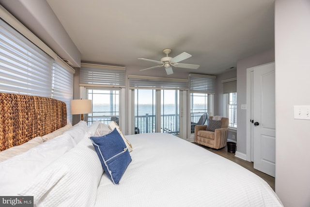 bedroom with access to exterior, hardwood / wood-style flooring, ceiling fan, and a water view