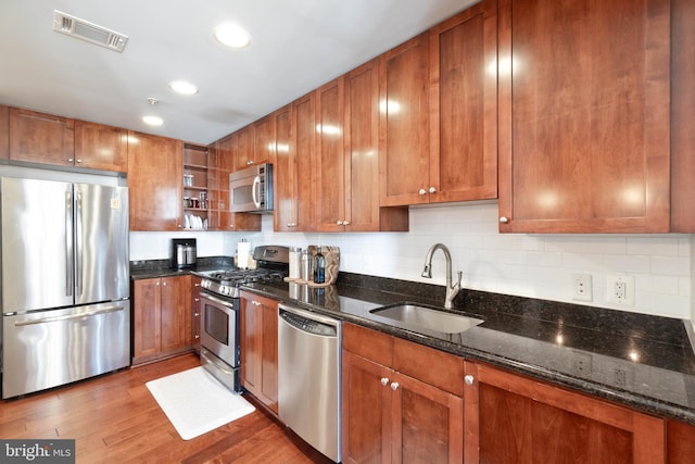 kitchen with light wood finished floors, visible vents, appliances with stainless steel finishes, a sink, and dark stone counters