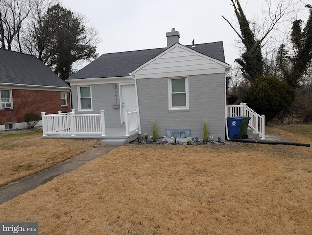 bungalow-style home with a shingled roof, a chimney, a wooden deck, a front lawn, and brick siding