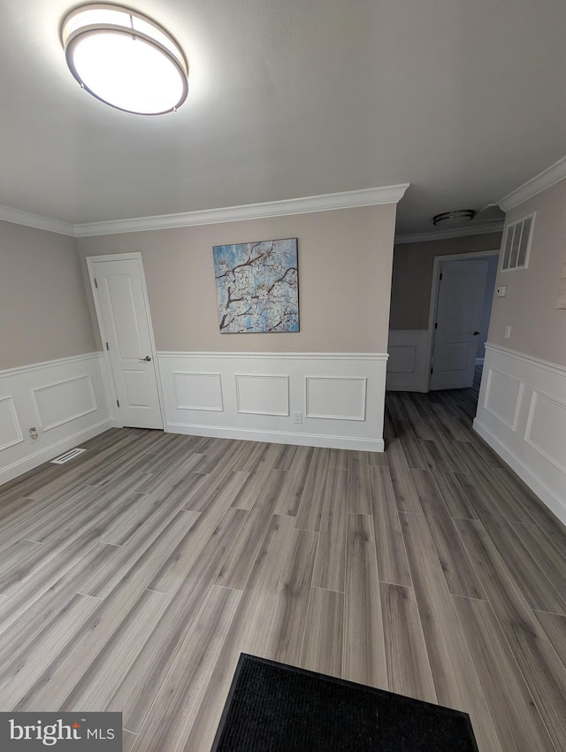 unfurnished room featuring ornamental molding, wainscoting, wood finished floors, and visible vents