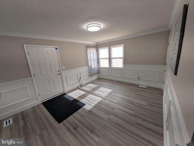 foyer entrance featuring visible vents, a decorative wall, wood finished floors, and ornamental molding