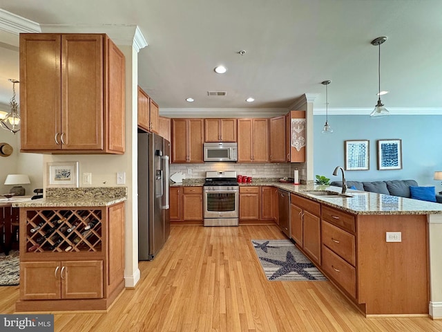 kitchen featuring visible vents, a peninsula, ornamental molding, a sink, and appliances with stainless steel finishes