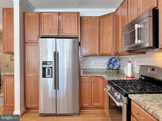 kitchen with decorative backsplash, stainless steel appliances, light wood-type flooring, and light stone countertops