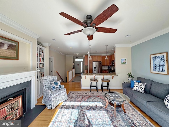 living area with ceiling fan, light wood-type flooring, and ornamental molding