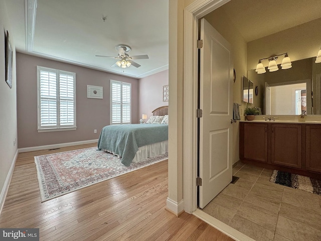 bedroom with visible vents, baseboards, ceiling fan, light wood-style flooring, and a sink