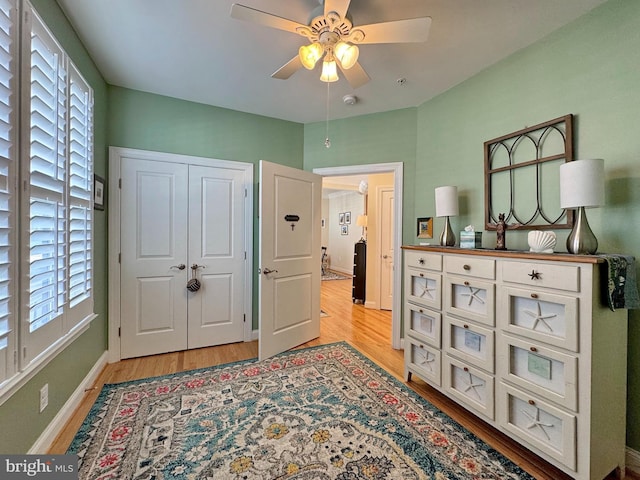 interior space featuring a ceiling fan, light wood-style floors, baseboards, and a closet