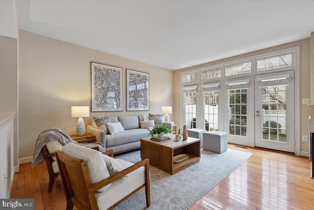 living room with light wood-style floors, visible vents, french doors, and baseboards