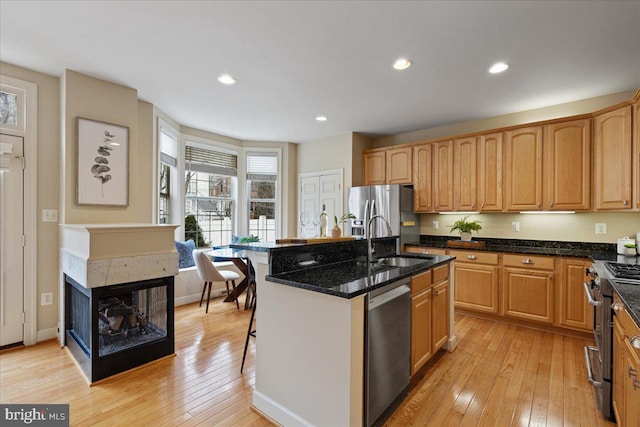 kitchen featuring a sink, dark stone counters, appliances with stainless steel finishes, light wood-style floors, and a kitchen island with sink