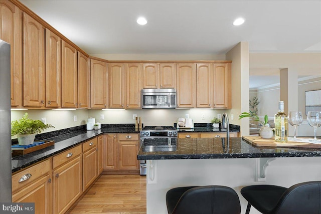 kitchen with a kitchen bar, dark stone countertops, light wood-style floors, stainless steel appliances, and a sink