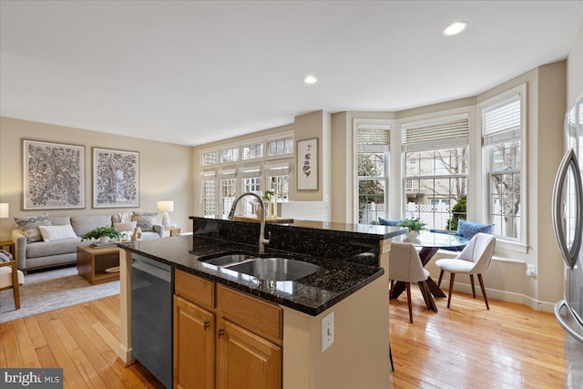 kitchen featuring a center island with sink, a sink, open floor plan, light wood-style floors, and dishwasher