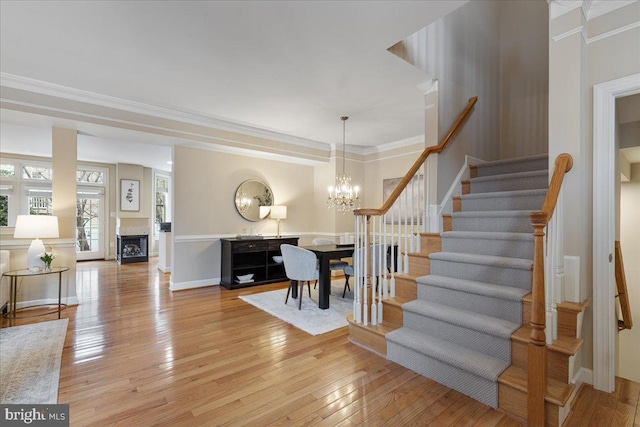 stairs featuring baseboards, a fireplace, ornamental molding, hardwood / wood-style flooring, and a notable chandelier