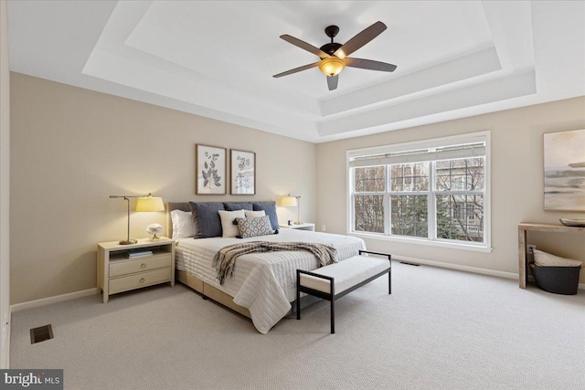 bedroom with light colored carpet, a raised ceiling, baseboards, and visible vents