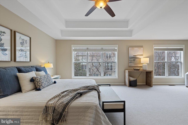 carpeted bedroom featuring visible vents, baseboards, a raised ceiling, and ceiling fan