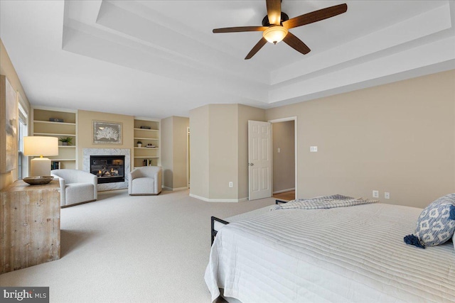 bedroom with ceiling fan, baseboards, carpet, a glass covered fireplace, and a raised ceiling