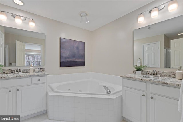 full bath featuring a tub with jets, two vanities, and a sink