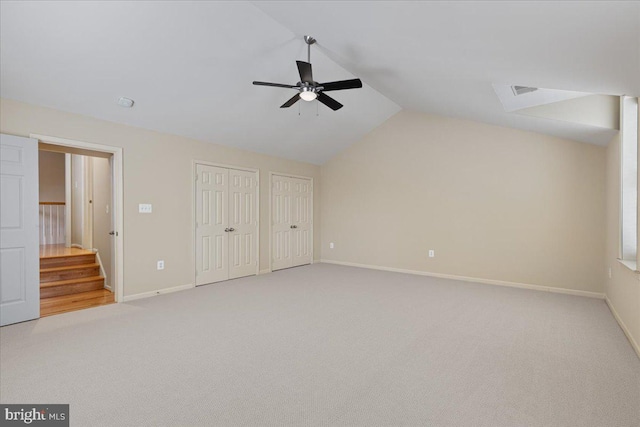 unfurnished bedroom featuring light carpet, two closets, baseboards, and vaulted ceiling