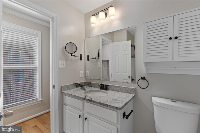 bathroom with vanity, toilet, wood finished floors, and baseboards