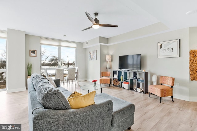 living room featuring ceiling fan, visible vents, light wood-style flooring, and baseboards