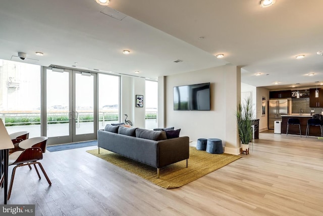 living area featuring light wood-style floors, baseboards, floor to ceiling windows, and french doors