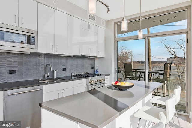 kitchen with stainless steel appliances, decorative backsplash, white cabinetry, a sink, and a kitchen bar