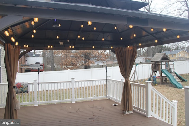 snow covered deck with a playground, a fenced backyard, and a gazebo