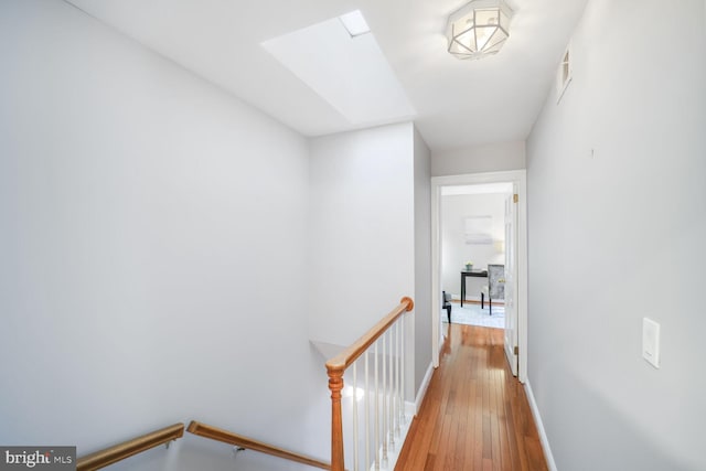 hall with a skylight, visible vents, an upstairs landing, baseboards, and hardwood / wood-style floors