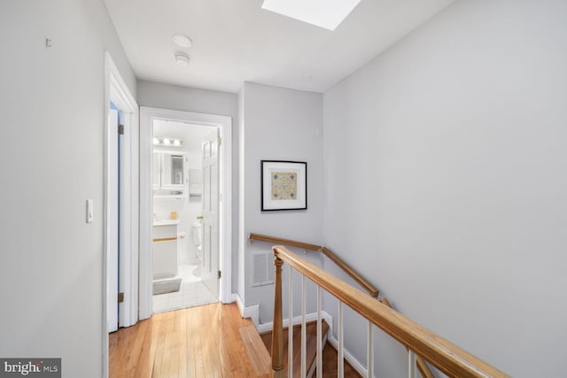 hall with an upstairs landing, a skylight, wood finished floors, and visible vents