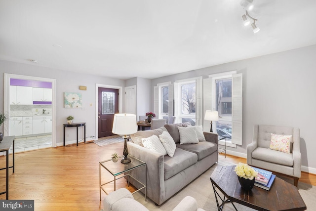 living room featuring light wood-type flooring, rail lighting, and baseboards