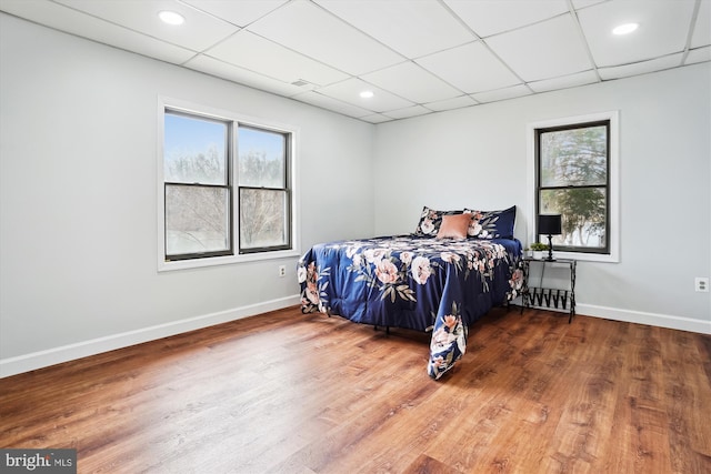 bedroom featuring a paneled ceiling, hardwood / wood-style floors, and multiple windows