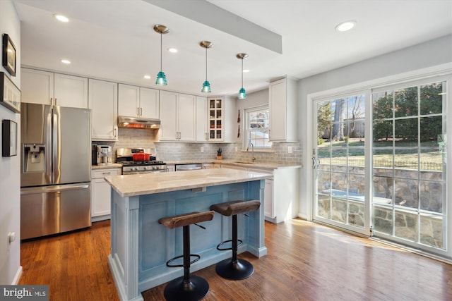 kitchen with appliances with stainless steel finishes, dark wood-type flooring, white cabinets, a sink, and under cabinet range hood