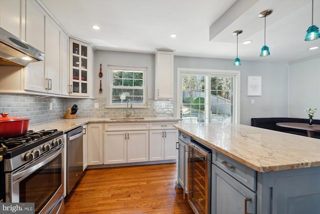 kitchen with light stone counters, extractor fan, beverage cooler, stainless steel appliances, and a sink