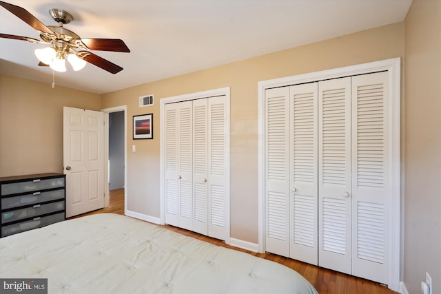 unfurnished bedroom featuring baseboards, visible vents, ceiling fan, wood finished floors, and two closets