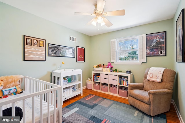 bedroom featuring a nursery area, baseboards, and wood finished floors