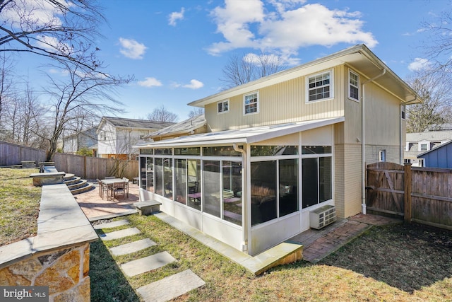 rear view of property with a patio, brick siding, a fenced backyard, and a sunroom